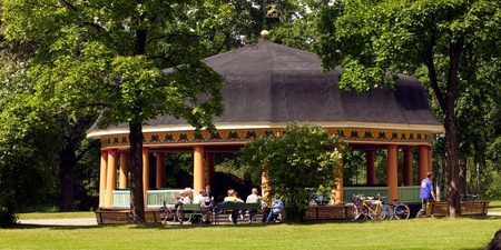 En paviljong i en grön park med människor som sitter vid bänkar och cyklar parkerade bredvid.