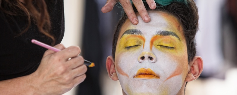 En person får ansiktsmålning med färgglada färger av en annan person, ögonen är slutna.