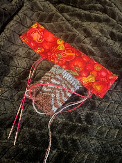 Stickning med mönstrat garn och rundstickor på en mörk filt, med ett fodral med tomatmönster.