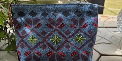 Liten blå tygväska sydd av jeans, med handtryck broderat mönster i rött och grönt, placerad på ett bord med betongskiva..