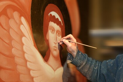 En person målar ett religiöst motiv av en ängel med vingar på en ikonliknande tavla.