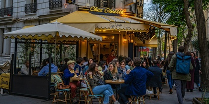 Uteservering på ett franskt café med människor som samtalar och äter under en gul markis.