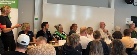 Paneldebatt med flera personer sittande vid ett bord och publik framför, i ett klassrum.