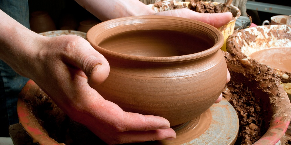 Två händer formar en lerkruka på en drejskiva i en keramikverkstad.
