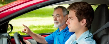 En ung man kör bil med en äldre man som passagerare, troligen under en körlektion.