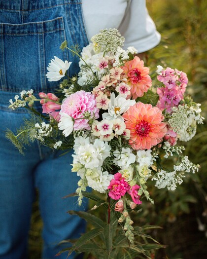En person i jeanskläder håller en färgglad bukett med blandade blommor utomhus.