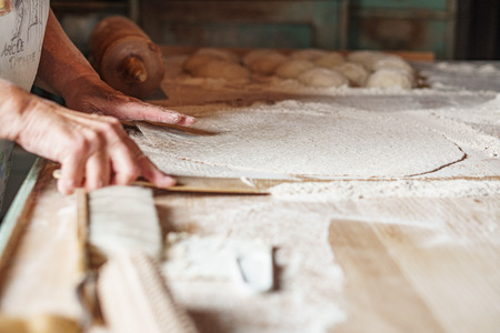 En person kavlar ut deg på ett mjölat bakbord med flera degbollar i bakgrunden.