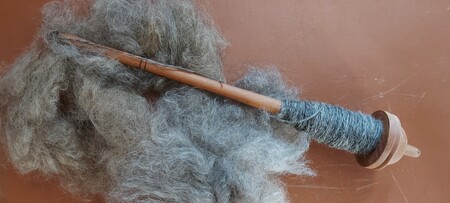 En slända med spunnet garn ligger på en hög av grå ull mot en brun bakgrund.