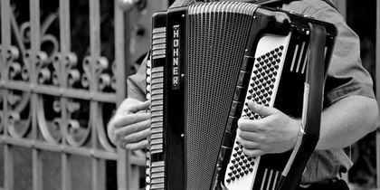En person spelar dragspel utomhus, bilden är i svartvitt och visar endast överkroppen och instrumentet.