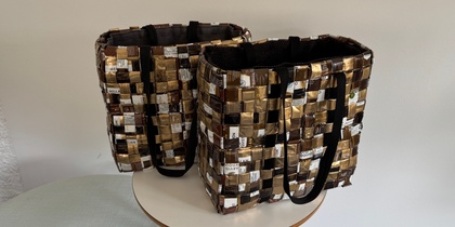 Två väskor flätade av återvunna kaffeförpackningar står på ett runt bord mot en vit vägg.