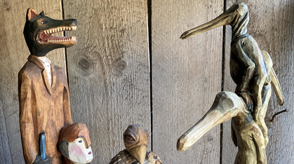 Träskulpturer föreställande djur och människor står mot en trävägg.