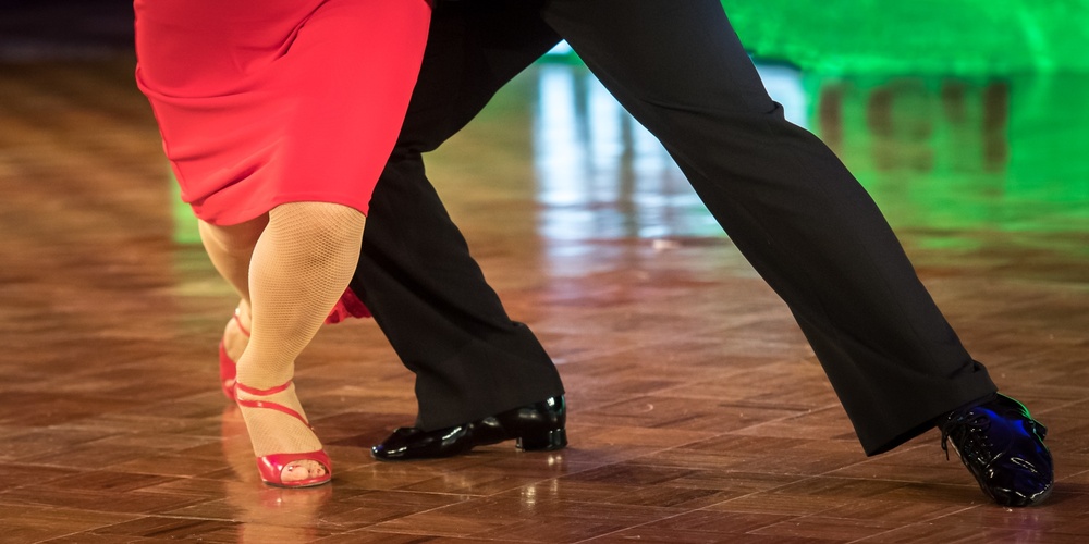 Två personer dansar tillsammans på ett dansgolv, endast deras ben och fötter syns.