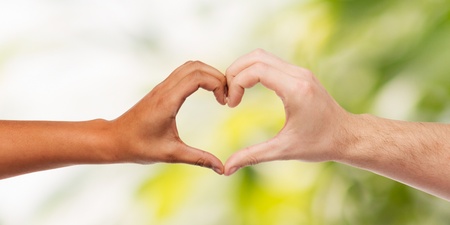 Två händer i olika hudtoner formar ett hjärta mot en suddig grön bakgrund.