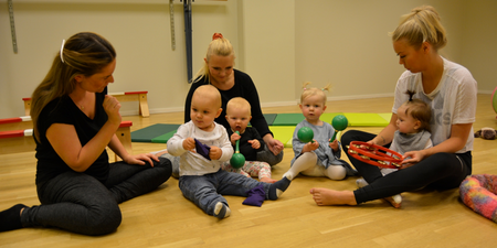 Tre vuxna och fyra små barn sitter på golvet i ett ljust rum och leker med musikinstrument.
