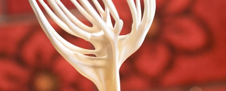 En visp med smet droppar ner i en gul skål, med röd bakgrund med blommönster.