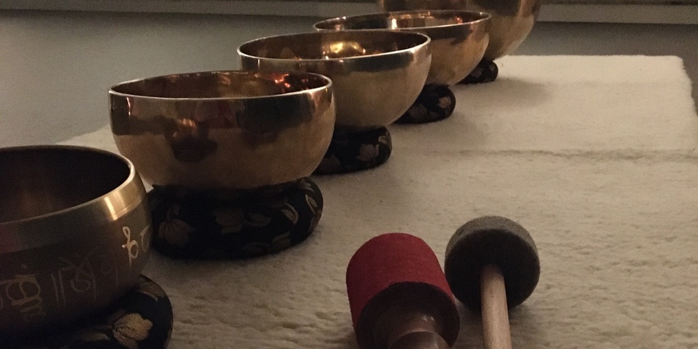 Fem tibetanska klangskålar står på rad på en matta med två klubbor framför dem i ett dämpat rum.