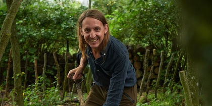 Person arbetar med en grep i en kompostbehållare i en grönskande trädgård.