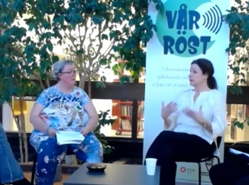Fyra personer sitter i en paneldiskussion inomhus med gröna växter och en banner i bakgrunden.