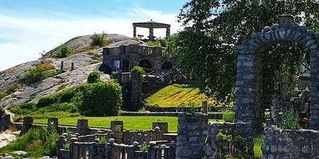 Stenbyggnader och valv på en grön kulle vid havet under en klarblå himmel.