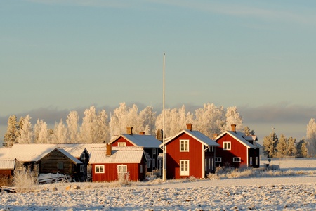 Röda trähus på snötäckt landsbygd med frostiga träd i bakgrunden under klar himmel.