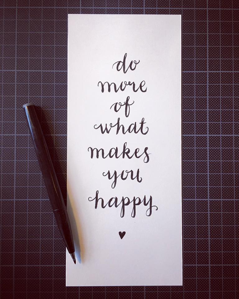 Handskriven text på ett vitt papper med budskapet 'do more of what makes you happy' och en penna bredvid.
