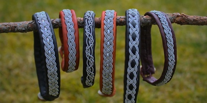 Sex armband med flätade mönster hänger på en gren utomhus med gräs i bakgrunden.