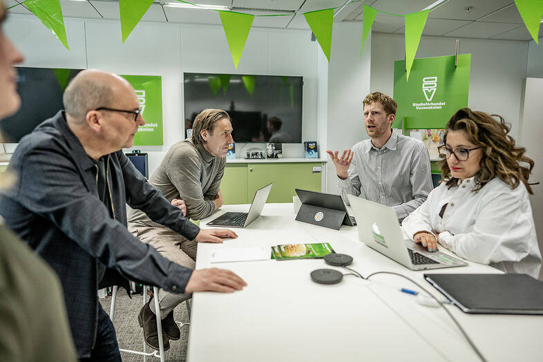En grupp personer sitter och arbetar runt ett bord.