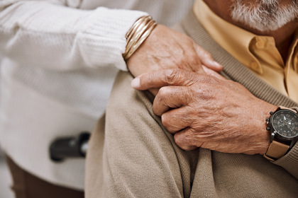 Två äldre personer håller varandra om axeln, närbild på händer och armar.