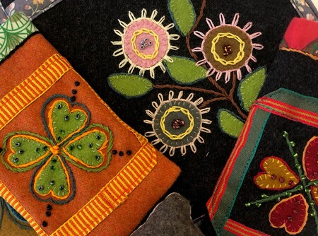 Färgglada broderier med blommor, hjärtan och ett fyrklöver på tygbitar i olika färger.