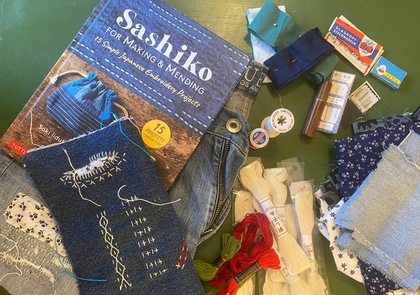 Material för sashiko-broderi, inklusive bok, trådar, tygbitar och nålar på ett bord.