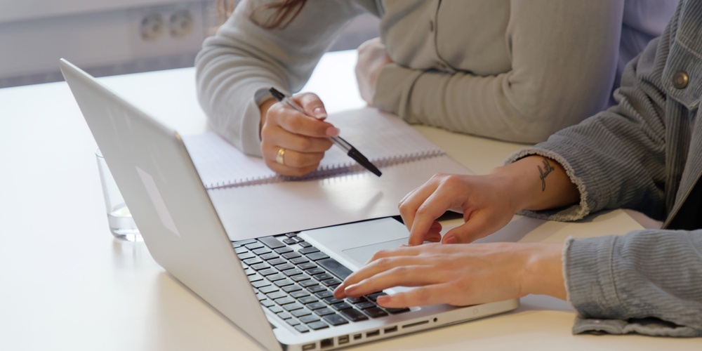 Två personer sitter vid ett bord, en skriver på en laptop och den andra antecknar i ett block.