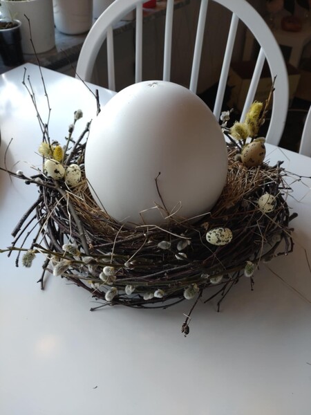 Stor vit dekorationsägg i ett fågelbo av kvistar och små prydnadsägg på ett vitt bord.