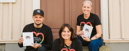 Tre personer sitter på en trappa utomhus och håller böcker med texten 'DANCE YOUR WAY'.