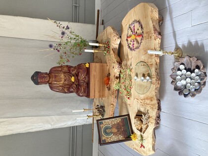 Ett buddhistiskt altare med staty, blommor, ljus, rökelse och en bild på Buddha på träbord.