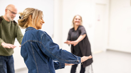 Tre vuxna personer deltar i en rörelse- eller dansövning i ett ljust rum.