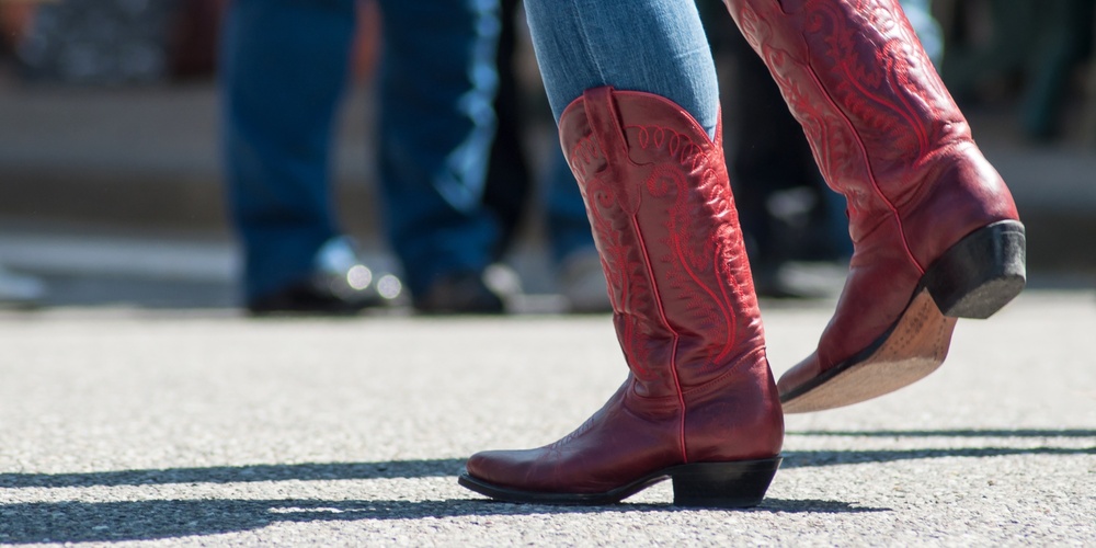 Person i blå jeans och röda cowboyboots dansar utomhus på asfalt.