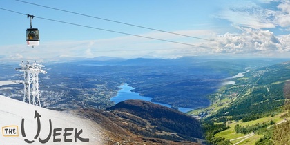 Landskapsvy med linbana över snötäckta och gröna berg, sjö och blå himmel.