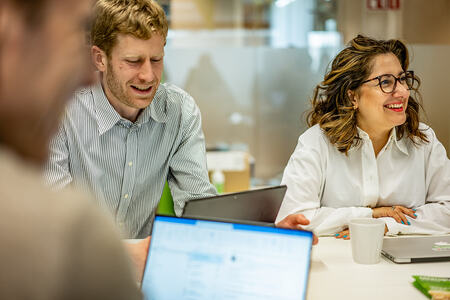 Tre personer sitter runt ett bord och arbetar med datorer.