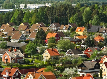 Färgglada villor med röda och gula tak i ett lummigt bostadsområde, omgivna av skog och berg i bakgrunden.
