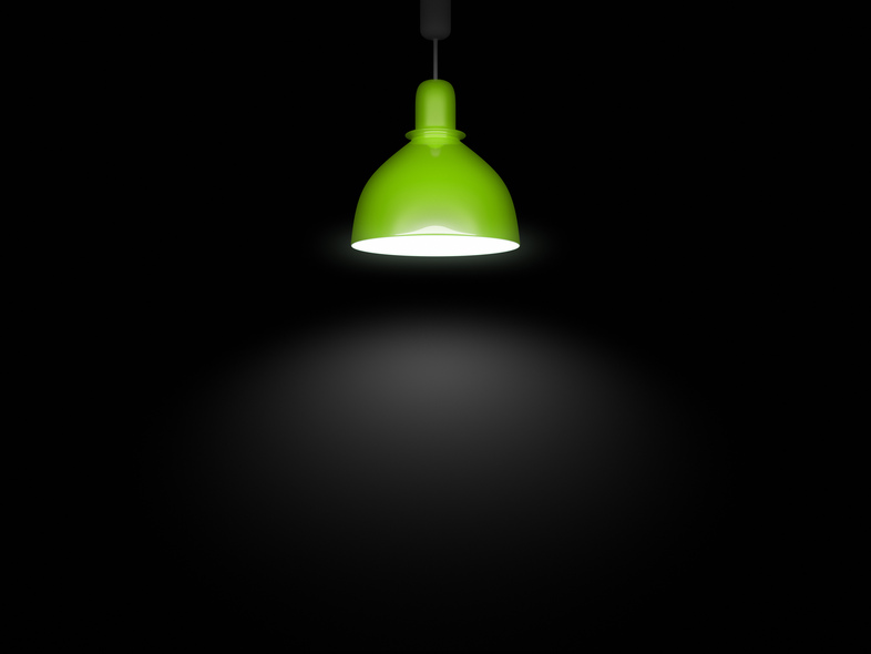En grön taklampa lyser upp ett mörkt rum med ett koncentrerat ljussken under sig.