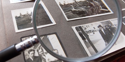 Ett fotoalbum med svartvita fotografier granskas med ett förstoringsglas.