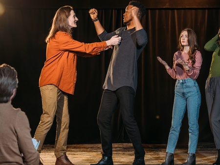 Fyra personer står på en scen och spelar teater, medan en person sitter och tittar på dem.