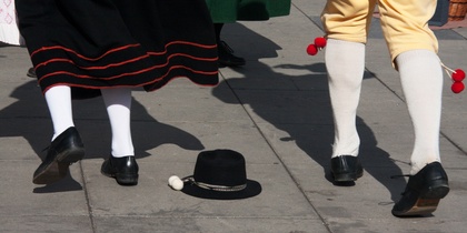 Två personer i traditionella folkdräkter dansar på en stenlagd yta, en svart hatt ligger på marken.