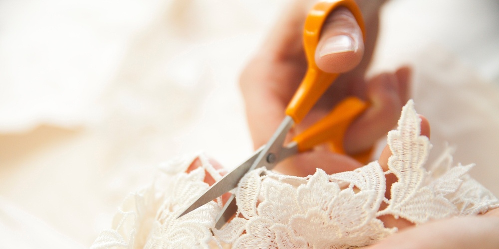 Närbild av händer som klipper vit spets med en sax.
