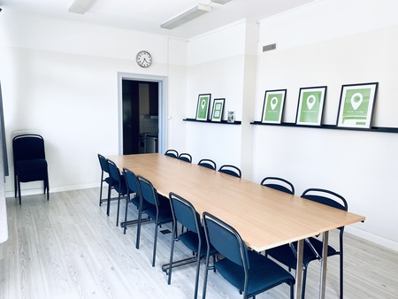 Ljust konferensrum med lång träbord, svarta stolar och gröna tavlor på väggen.