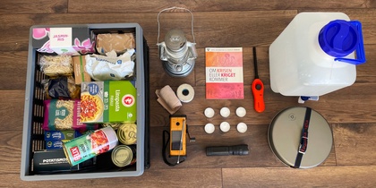 Nödkit med mat, vatten, ficklampa, stormlykta och första hjälpen på ett trägolv.