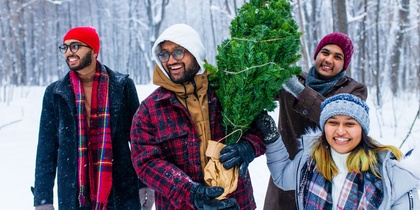 Fyra glada personer bär en julgran i en snöig skog, klädda i vinterkläder.