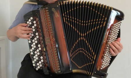 En person spelar på ett dragspel med många knappar och svart bälg.