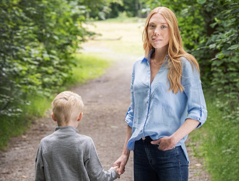 En kvinna och ett barn håller varandra i handen och promenerar på en skogsstig.