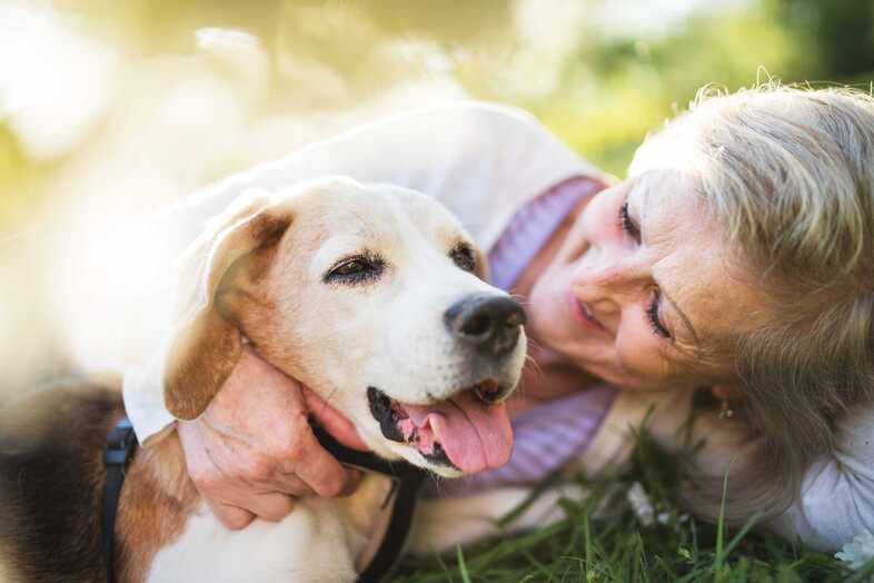 En äldre leende kvinna håller om en ljus hund.